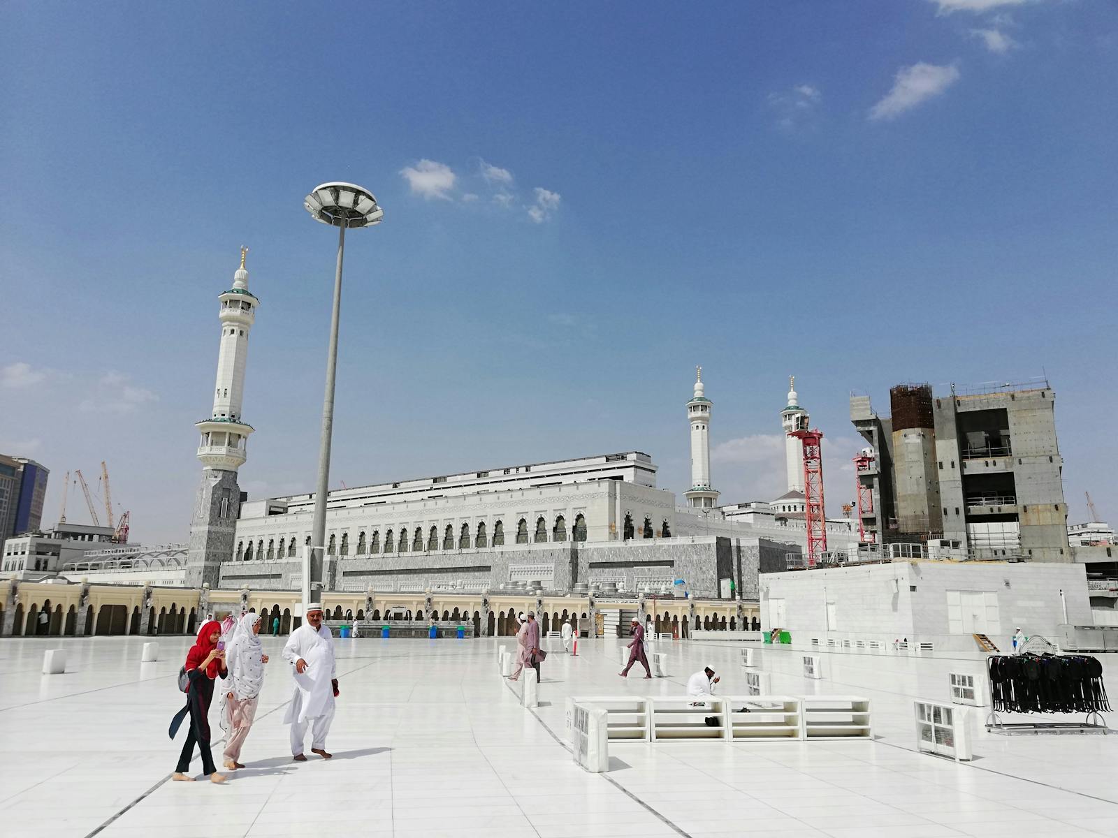 Pilgrims walk in the courtyard of Masjid al-Haram, Mecca, under a clear blue sky.