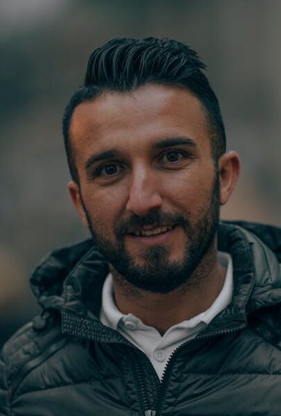 Cheerful bearded male in autumn jacket standing in city street and looking at camera
